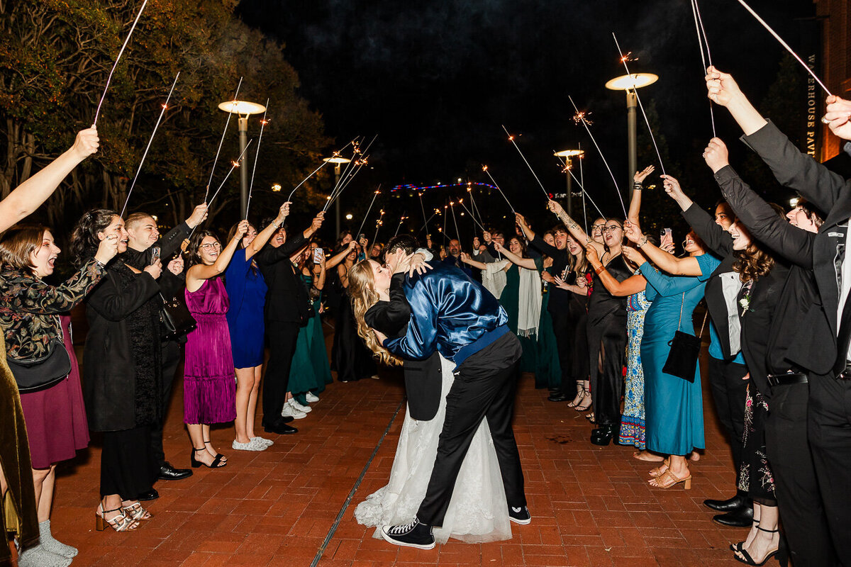 Bride and Groom kissing as guests gather around them with lit sparklers