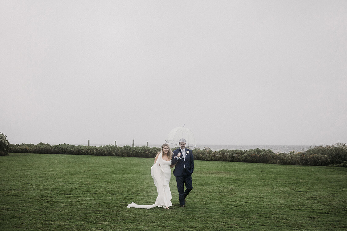 Bride and groom walk through misty lawn under an umbrella at a private estate on Great South Bay, Long Island. Photo by Mira Park Photography.