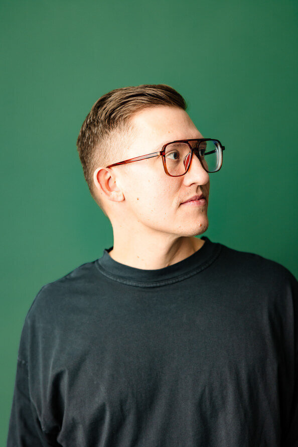 Man in glasses and green shirt on a green backdrop look up and to side.