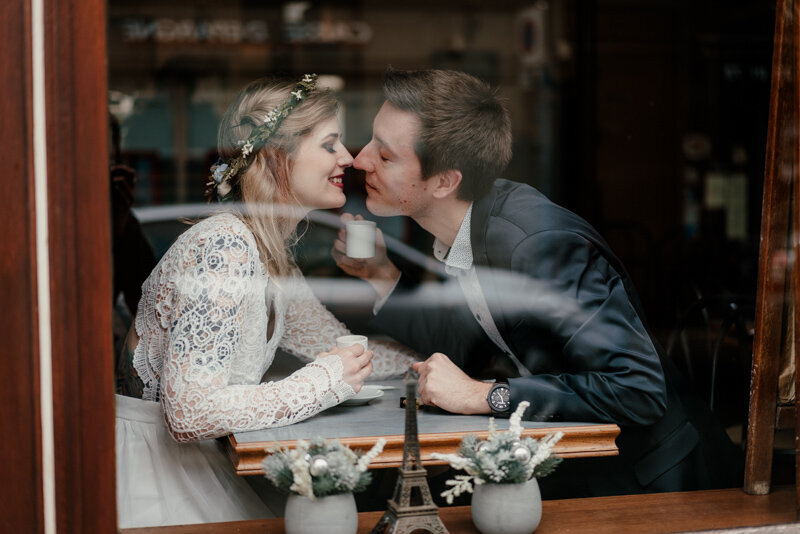 Moment suspendu dans un café parisien, les amoureux s’embrassent à travers la vitre, ambiance feutrée.
