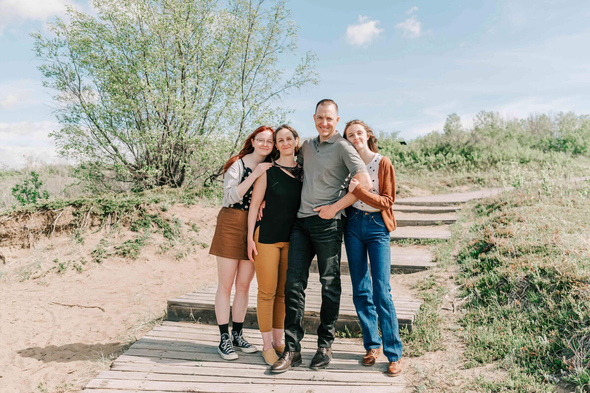 The family stands together on a wooden path with trees and bushes surrounding them. 