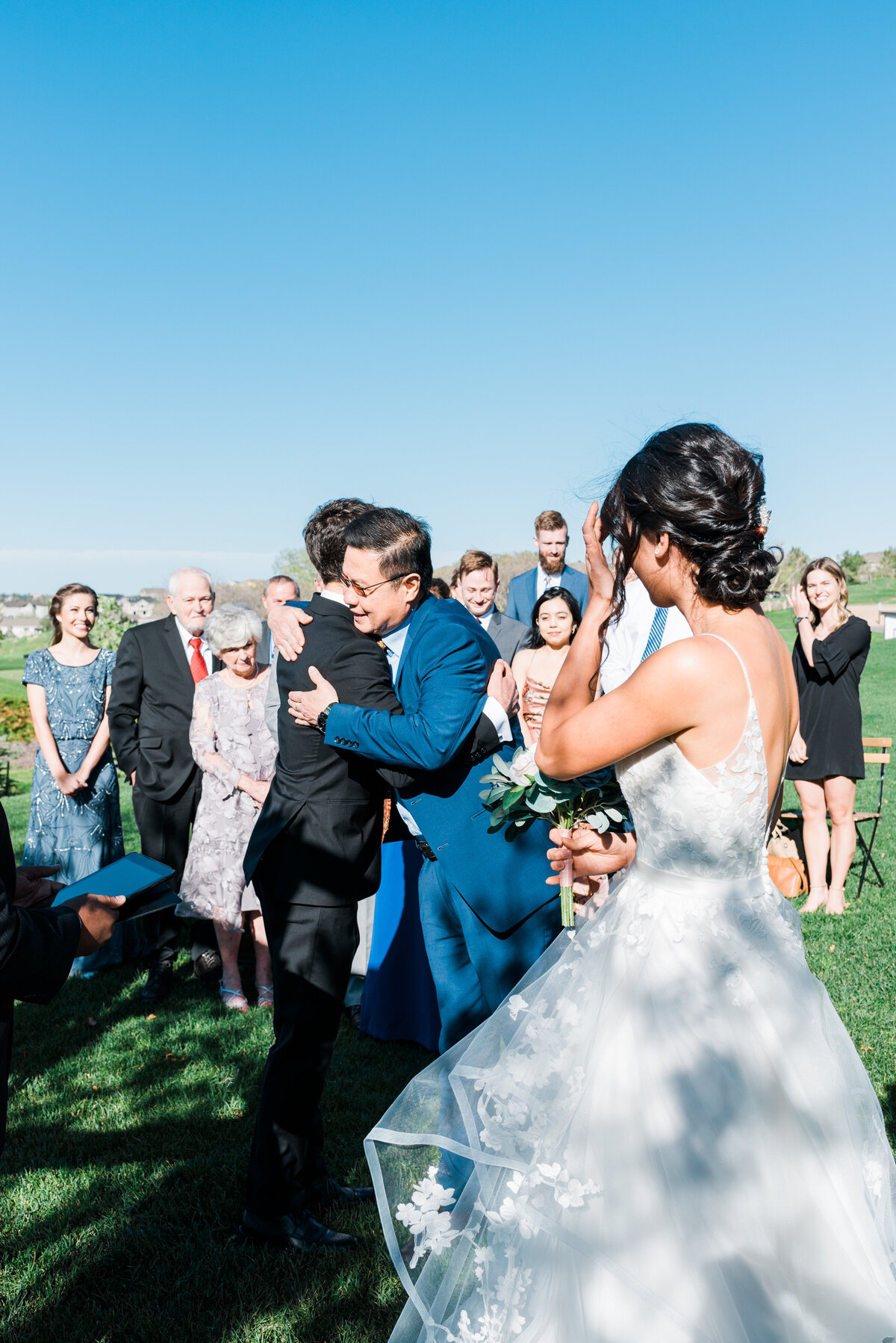 Denver wedding photographer captures father of the bride hugging the groom at the alter as he hands her off to be married at The Oaks wedding venue