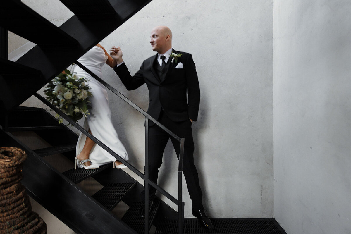 groom assists bride walking down stairs, she is not in full view