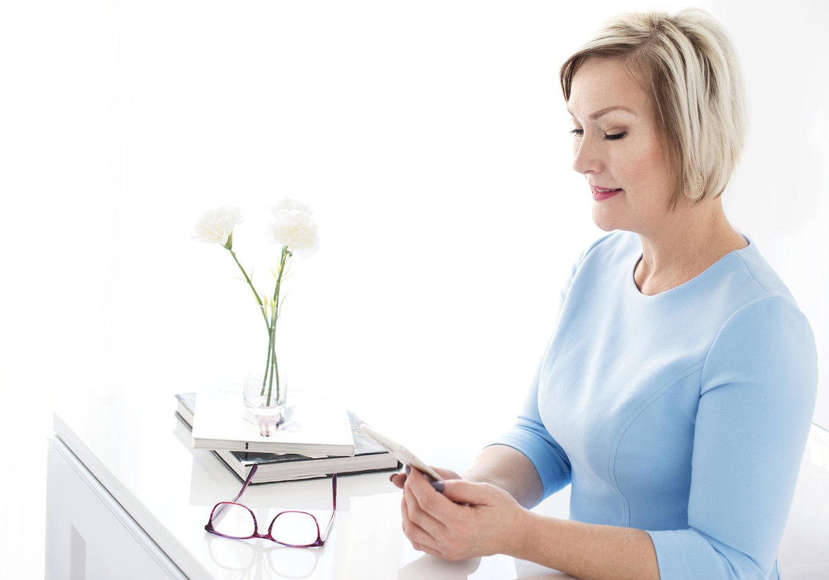 executive sitting on her office desk  eyeglasses on  desk looking at her phone