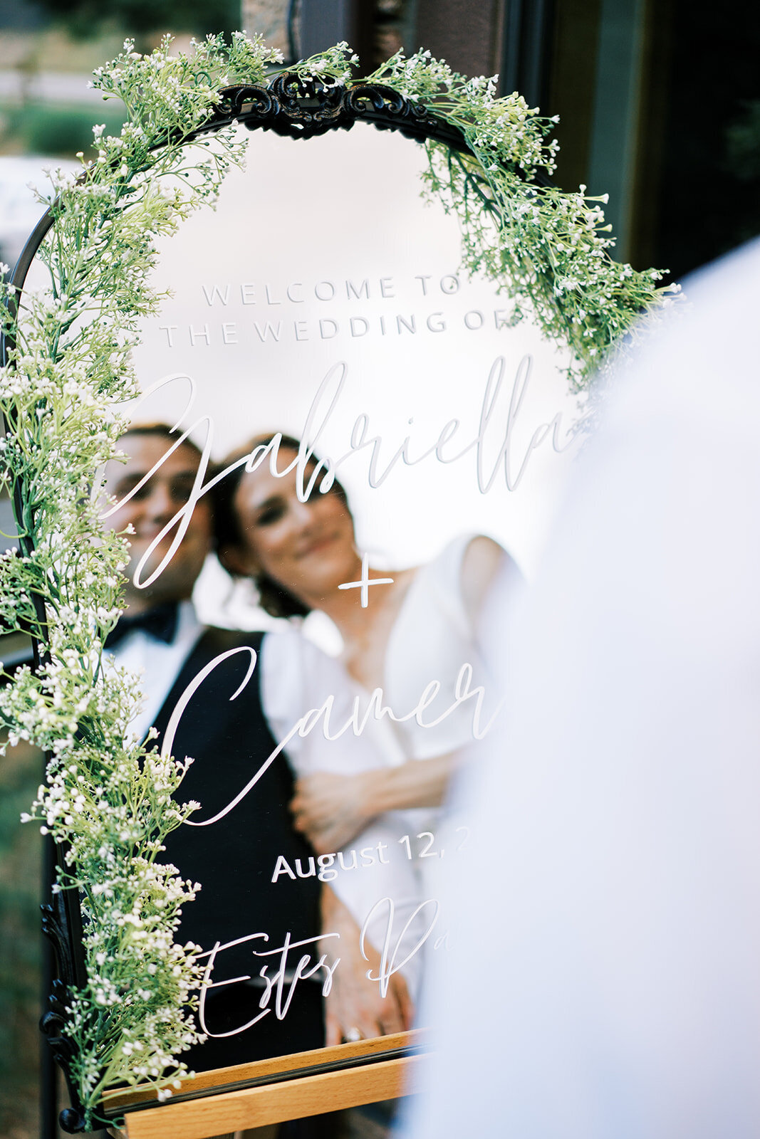 Bride and groom hug in the view of their mirror welcome sign .