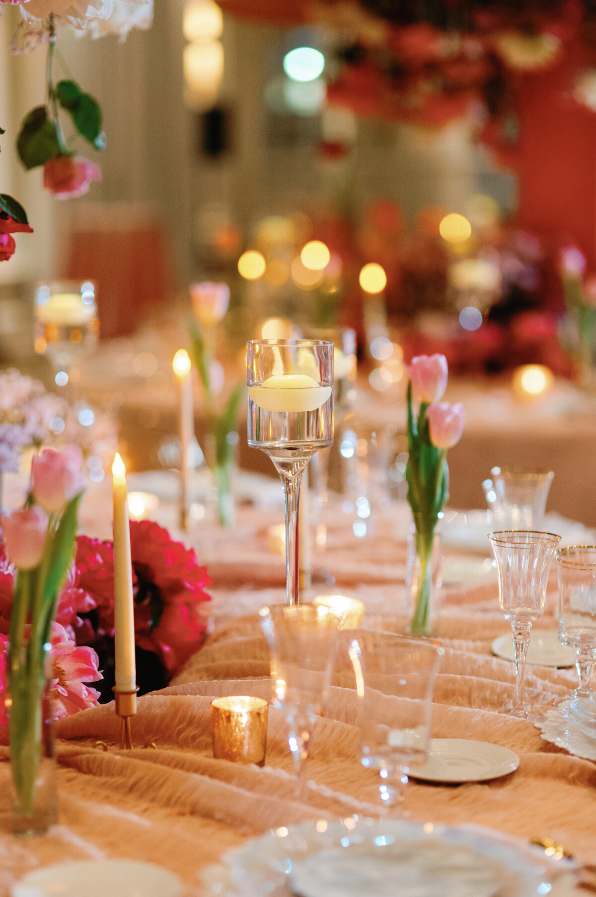 A dreamy and whimsical wedding tablescape adorned with delicate tulips and glowing candlelight. The soft floral arrangements and warm ambiance create an enchanting setting, perfect for couples seeking a romantic and elegant reception design.