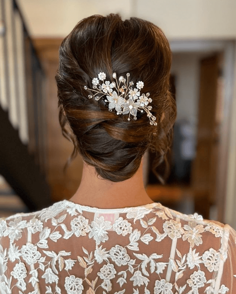 Elegant bridal low bun with pearl floral hairpiece styled for wedding hair and makeup in San Antonio