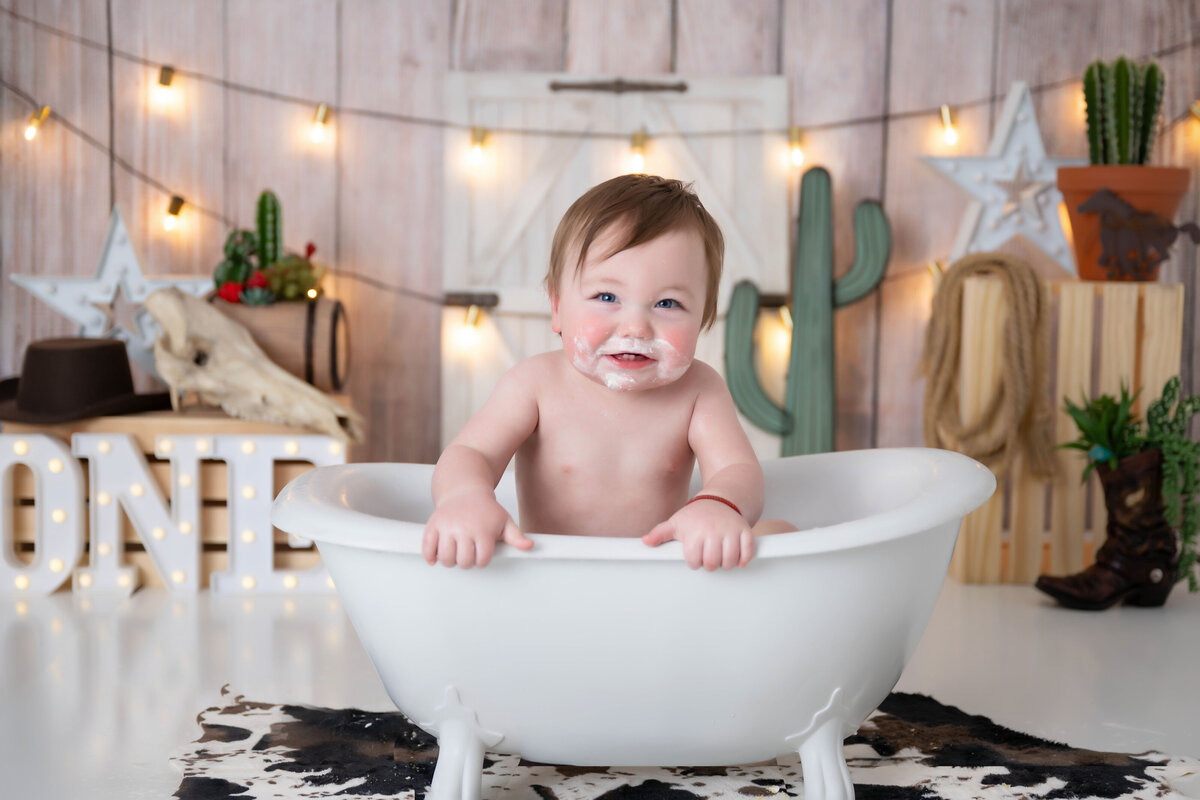Baby smiling while leaning near the edge of a mini tub placed over a cowhide rug.
