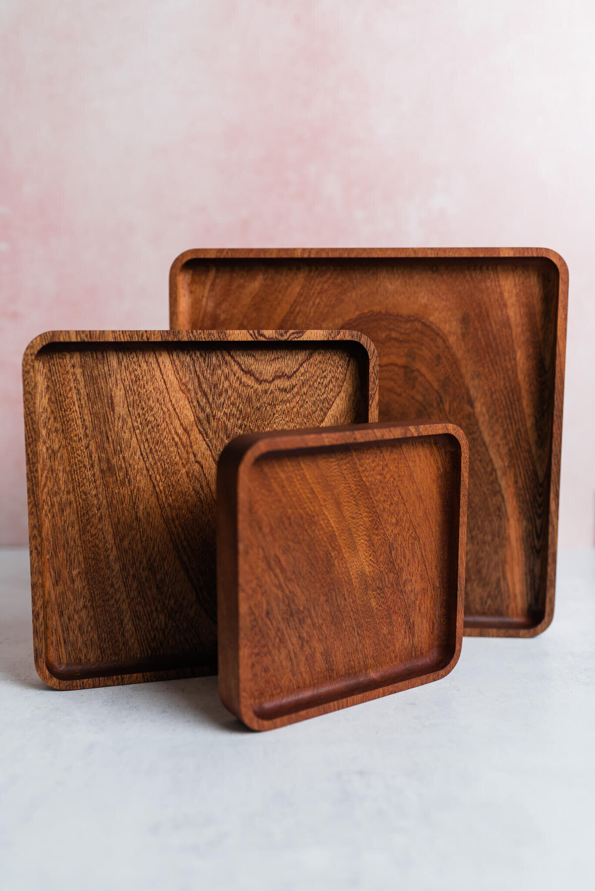 Wooden nesting trays stacked upright against a pink backdrop