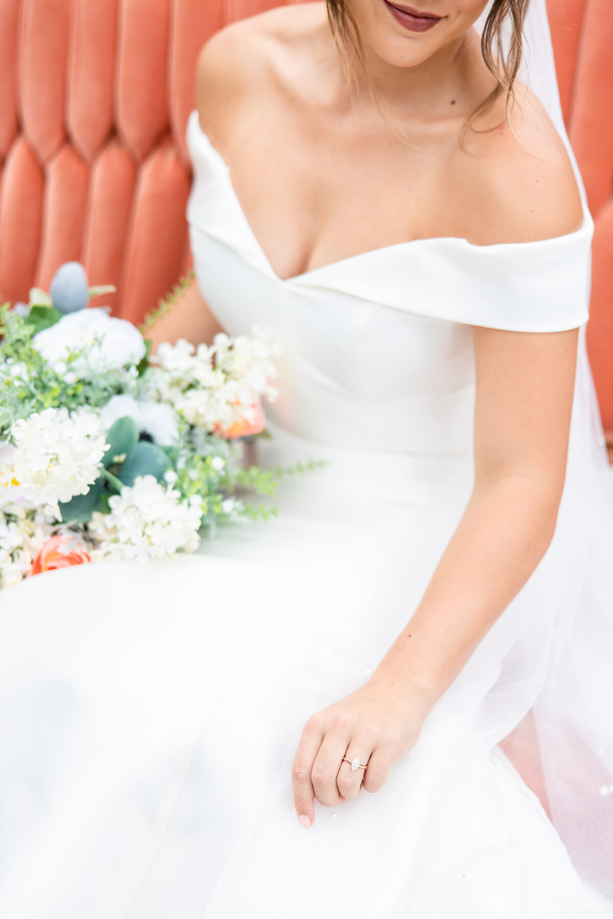 Bride holding her bright bouquet as she sits on a velvet bench