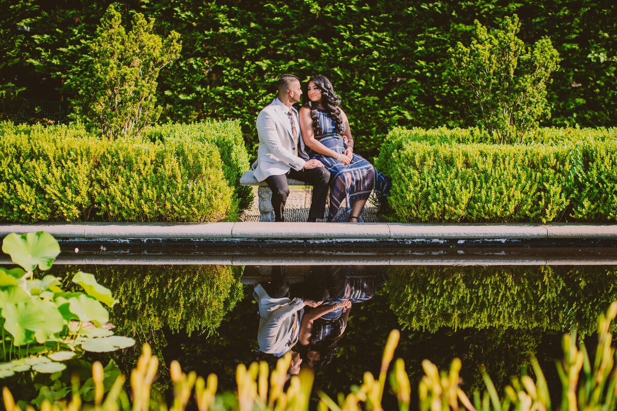 A couple sitting on a bench with their reflection in the pool at snug harbor garden in staten island in nyc