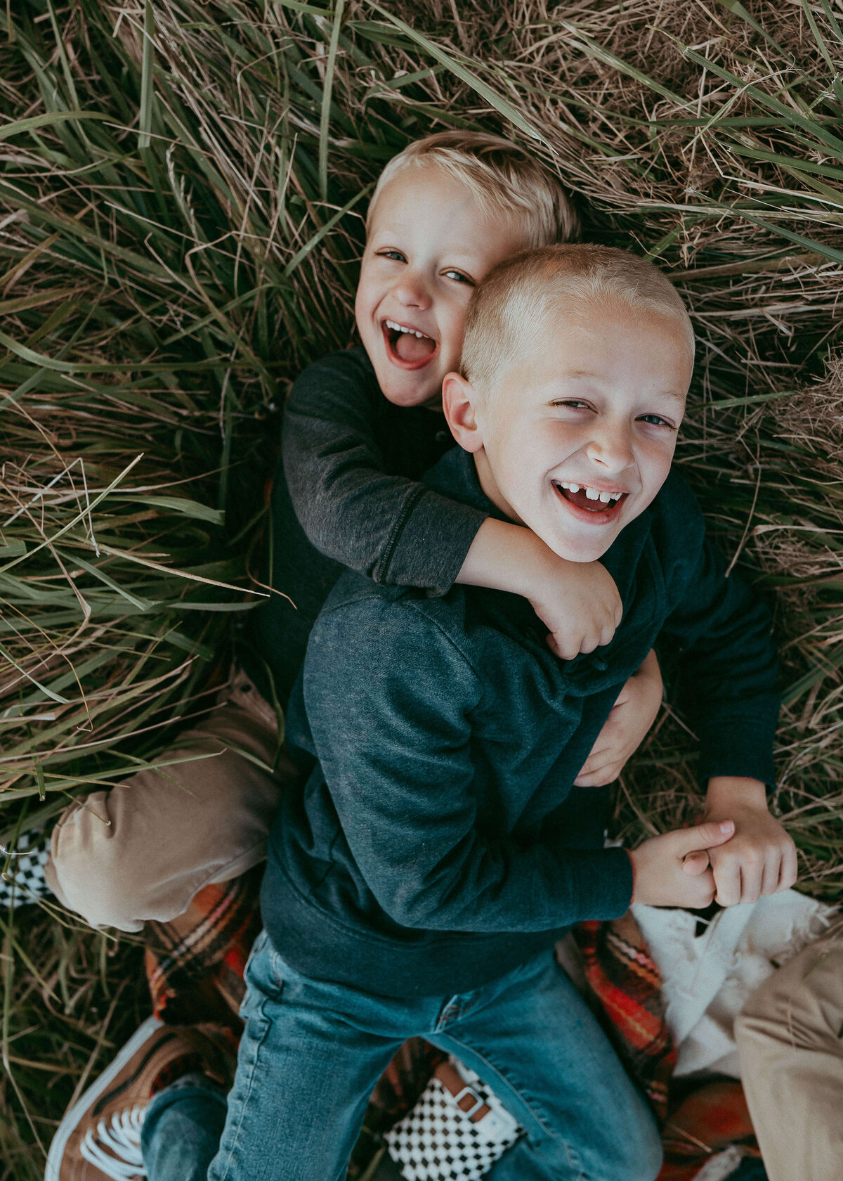 Two brothers wrestle in tall green grasses during a family photography session.
