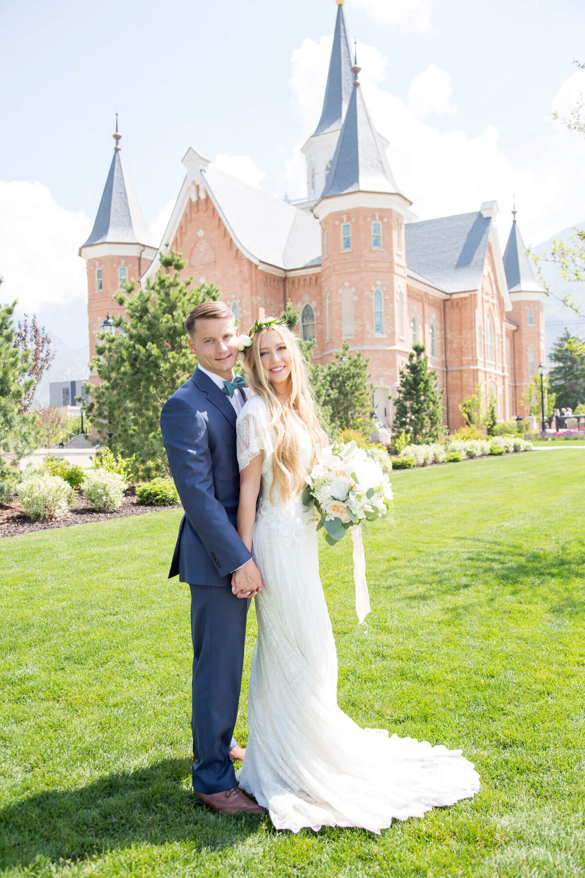 a bride and groom holding hands posing on grass by a brick building