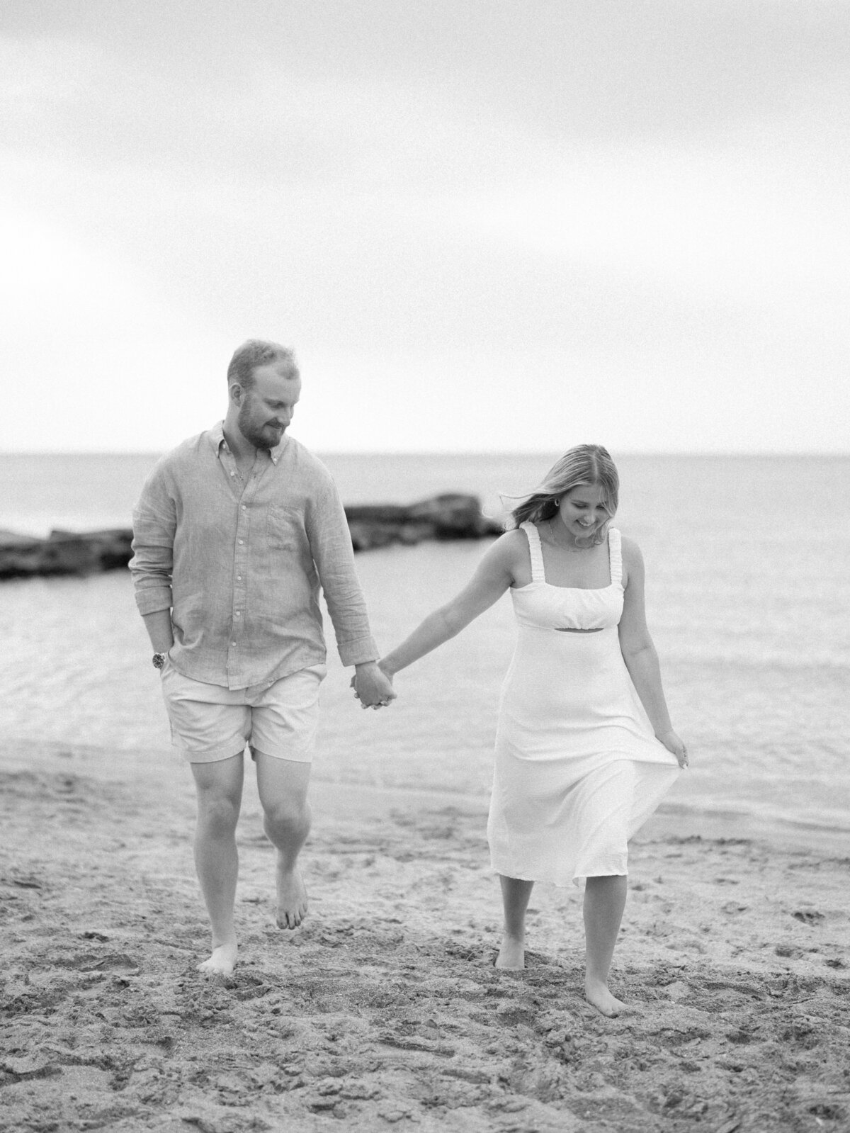 Couple holding hands walking barefoot on the sand during their Edgewater Beach engagement session.

