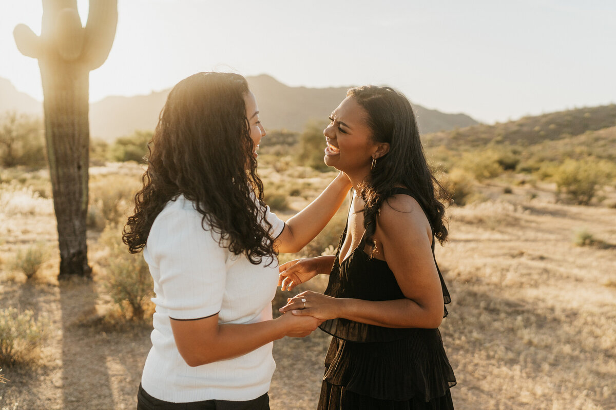 A couple laughing together as one has their hand on the other's shoulder 