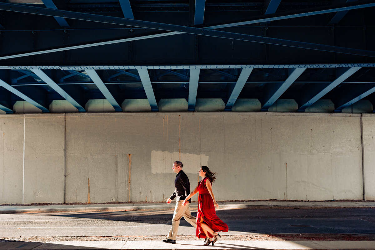 A couple walks holding hands under the high level bridge in toledo ohio.  Photo By Adore Wedding Photography. Toledo Wedding Photographers