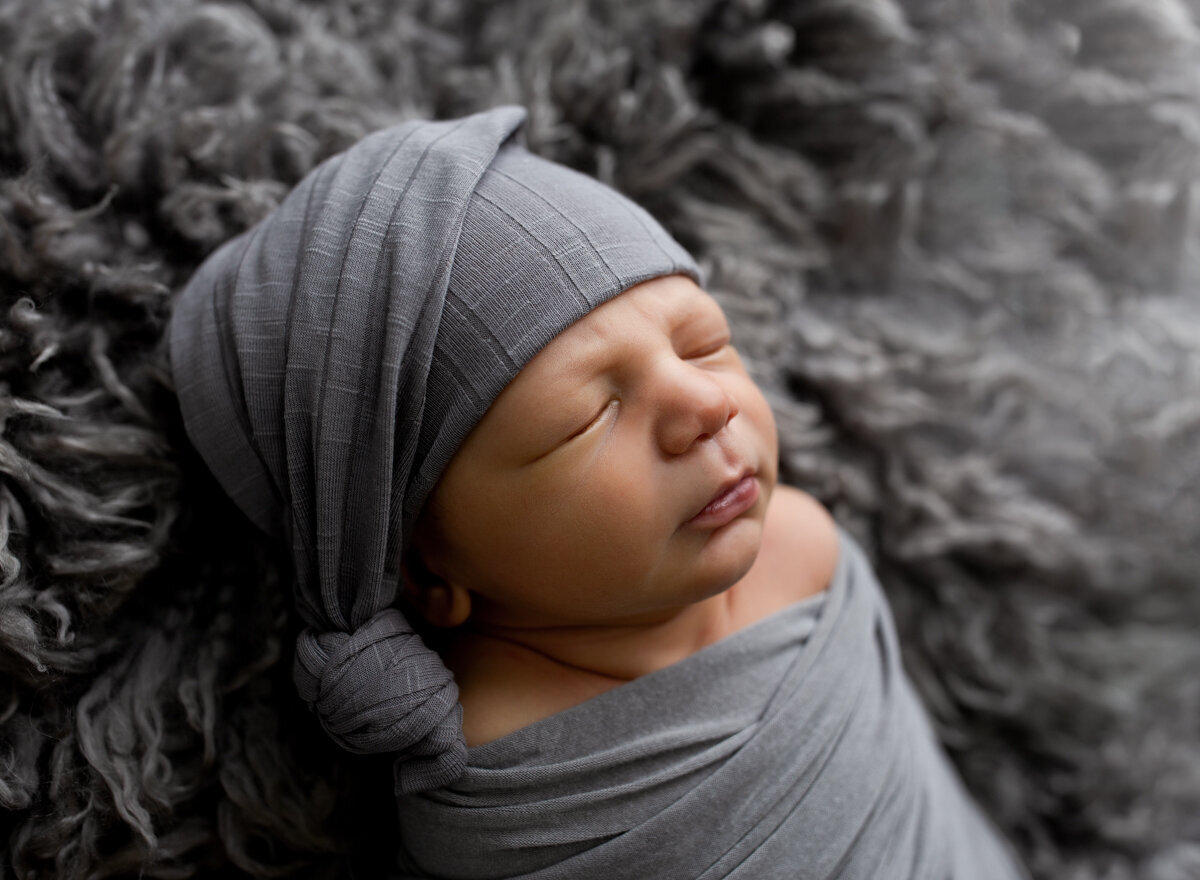 A profile of a sleeping baby boy on a grey fur.