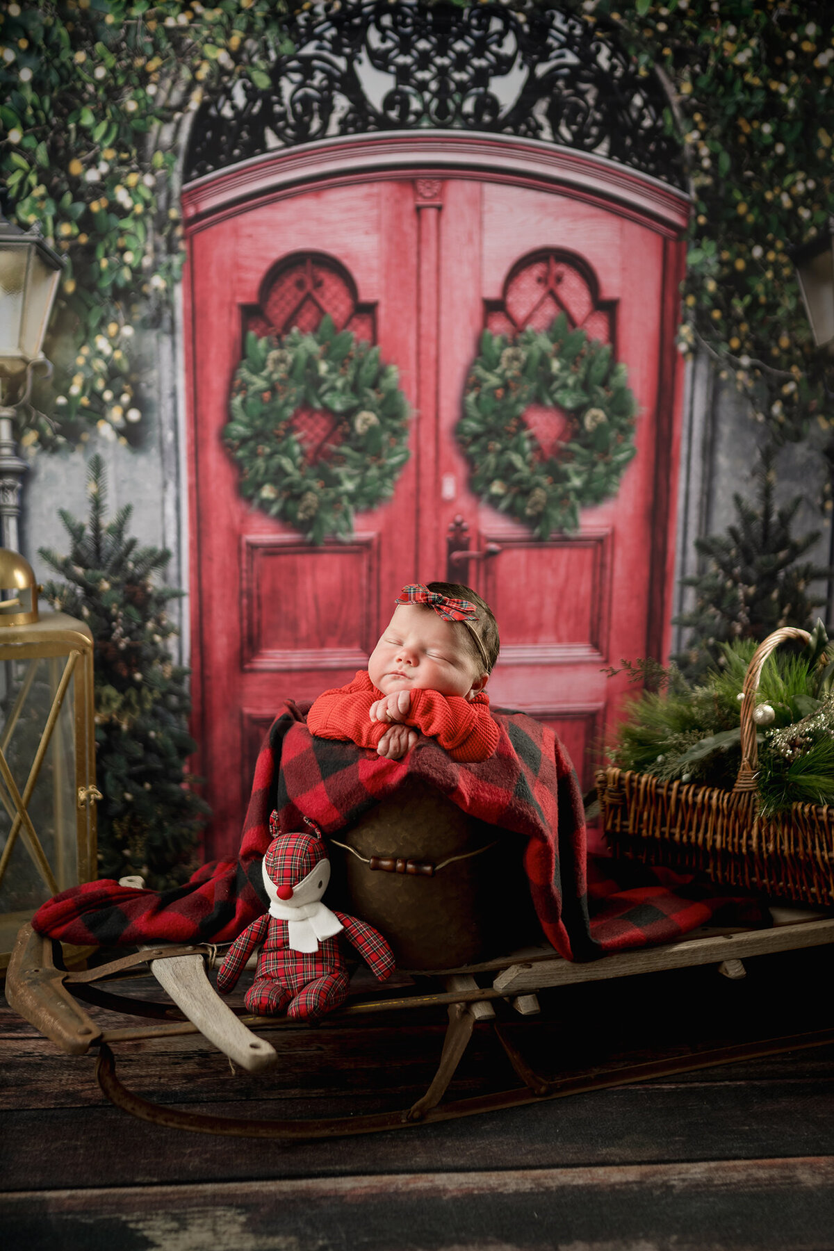 A newborn baby sleeps in a bucket on a sled in a christmas studio set