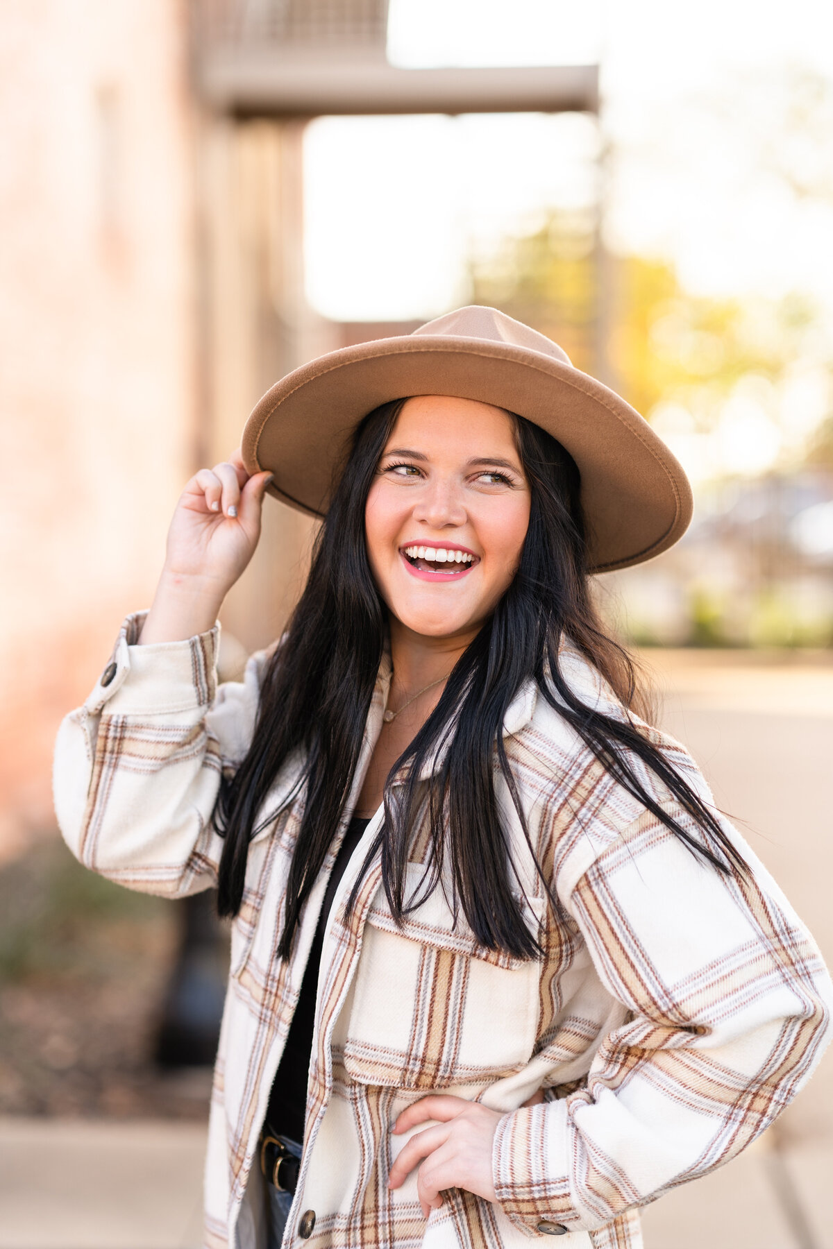 Girl wearing fall plaid and cute hat with hands on hip and hat while laughing off camera