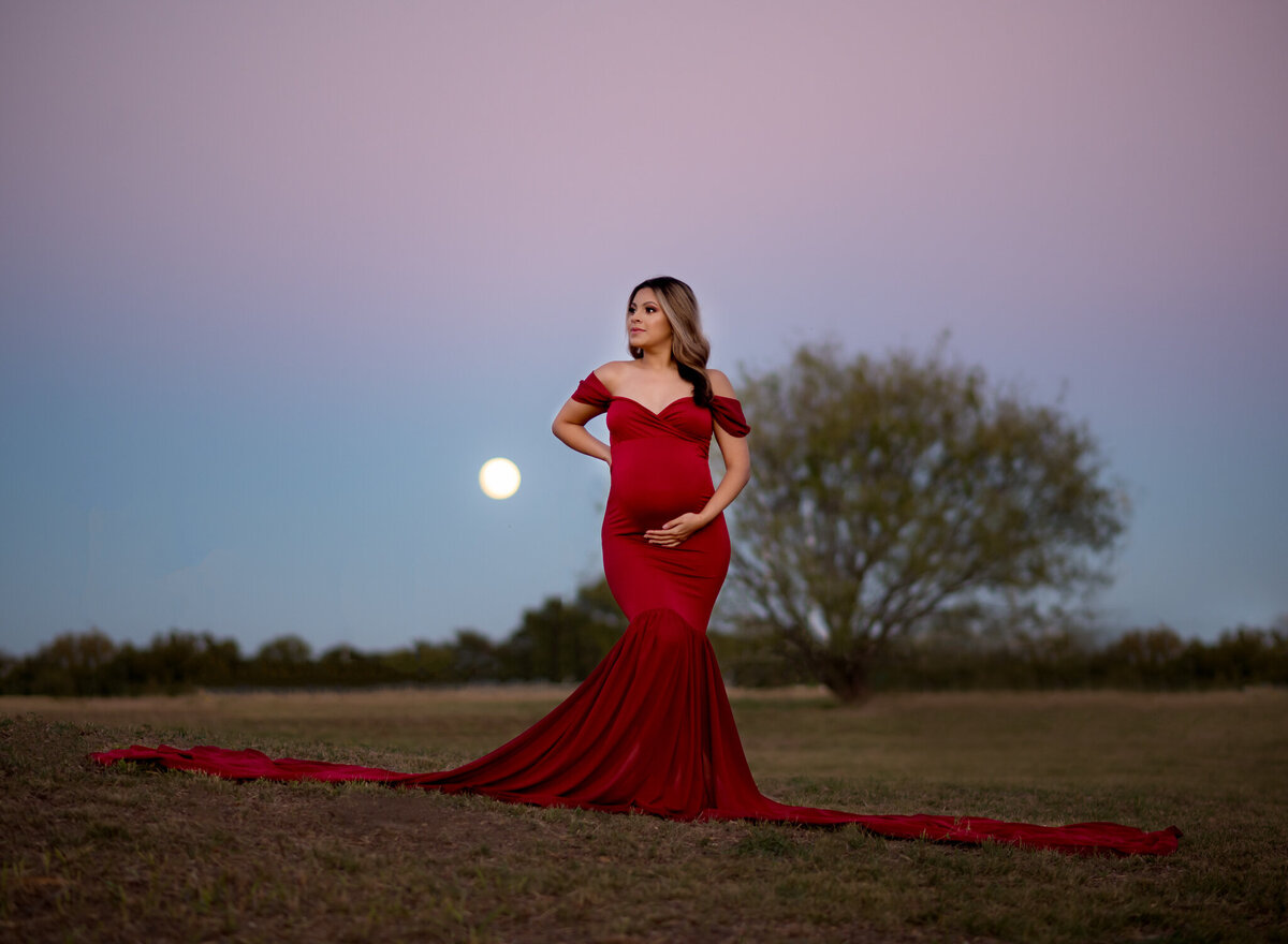 Outdoor maternity photo at dusk with full moon and flowing red gown near Westlake, Texas