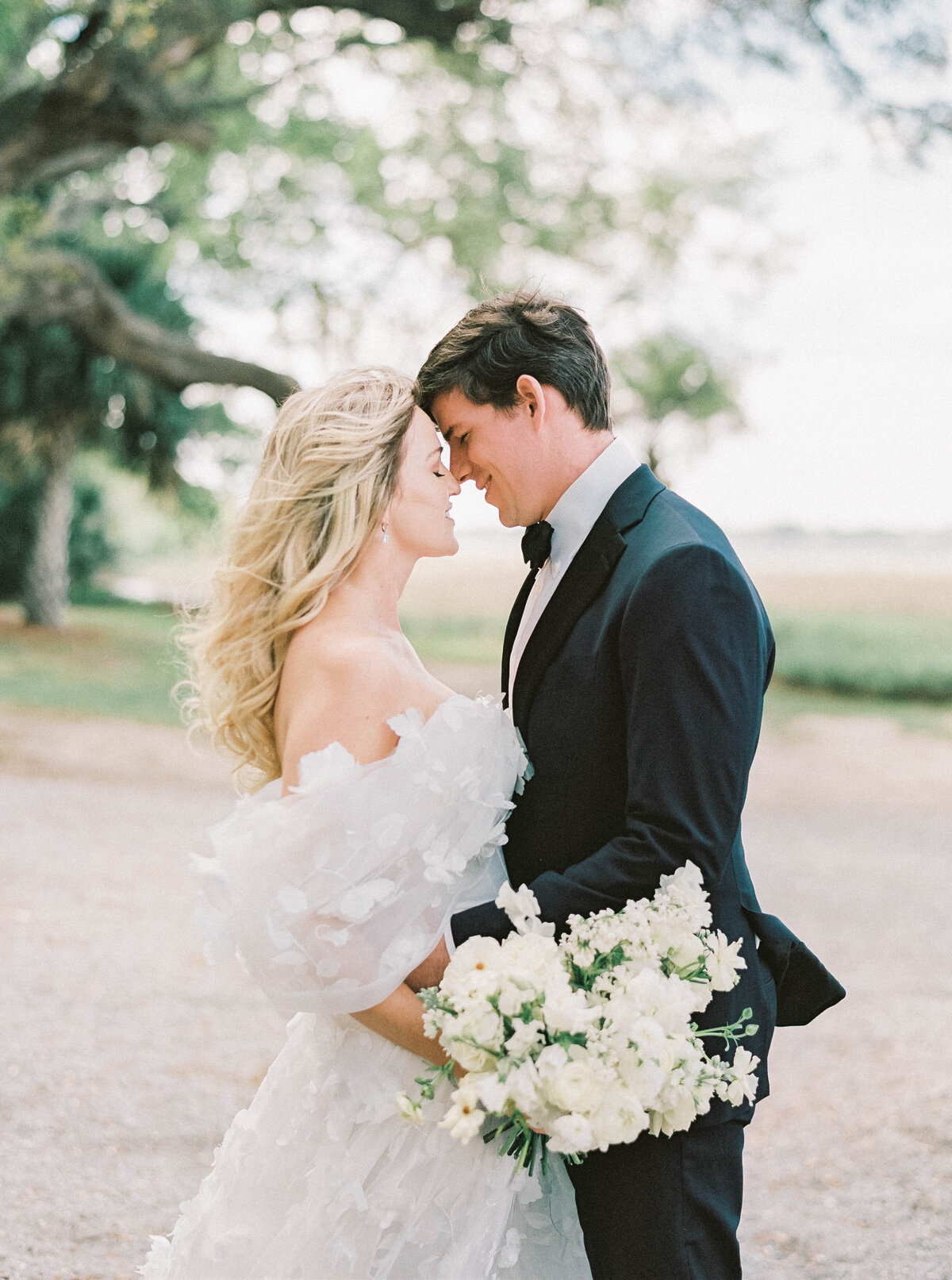 Newport Wedding Photographer | A bride and groom stand close, heads touching, smiling tenderly. The bride holds a bouquet of white flowers.