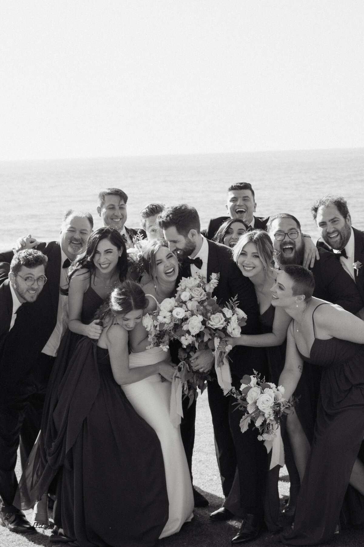 A joyful and candid moment with the bride, groom, and bridal party on the La Jolla cliffs, captured in an editorial wedding photography style.
