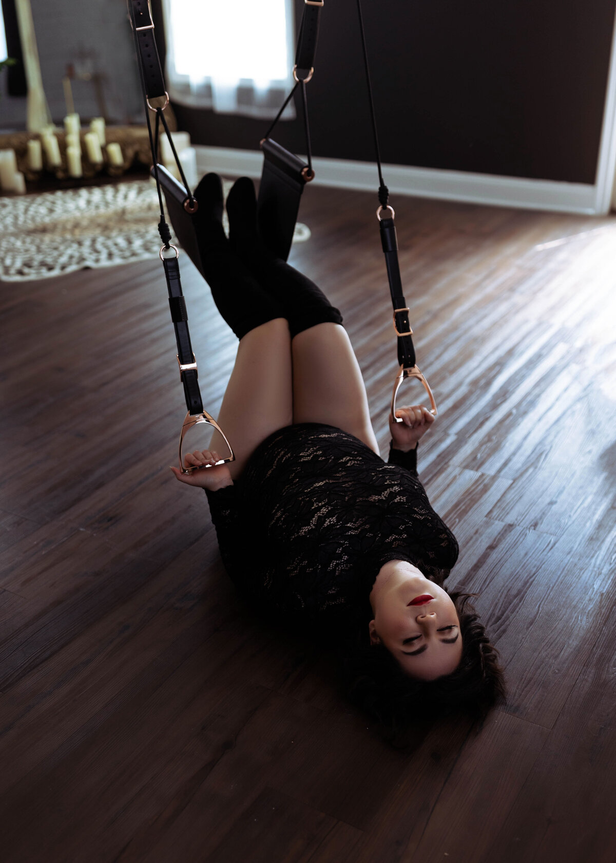 woman in black lingerie and heeled black boots laying on ground holding sex swing handles