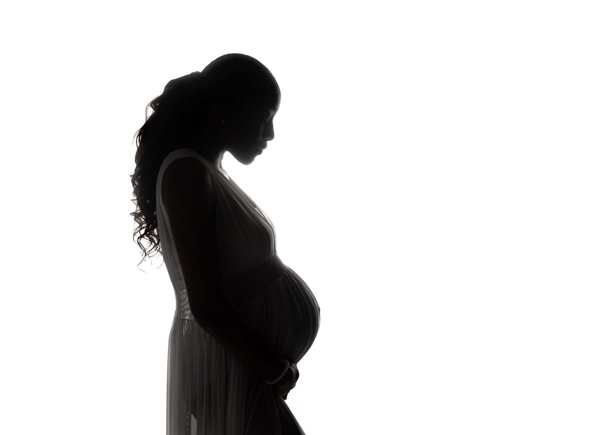 Silhouette of a mother to be gazing down at her bump while standing in a New Orleans Maternity Photographer studio