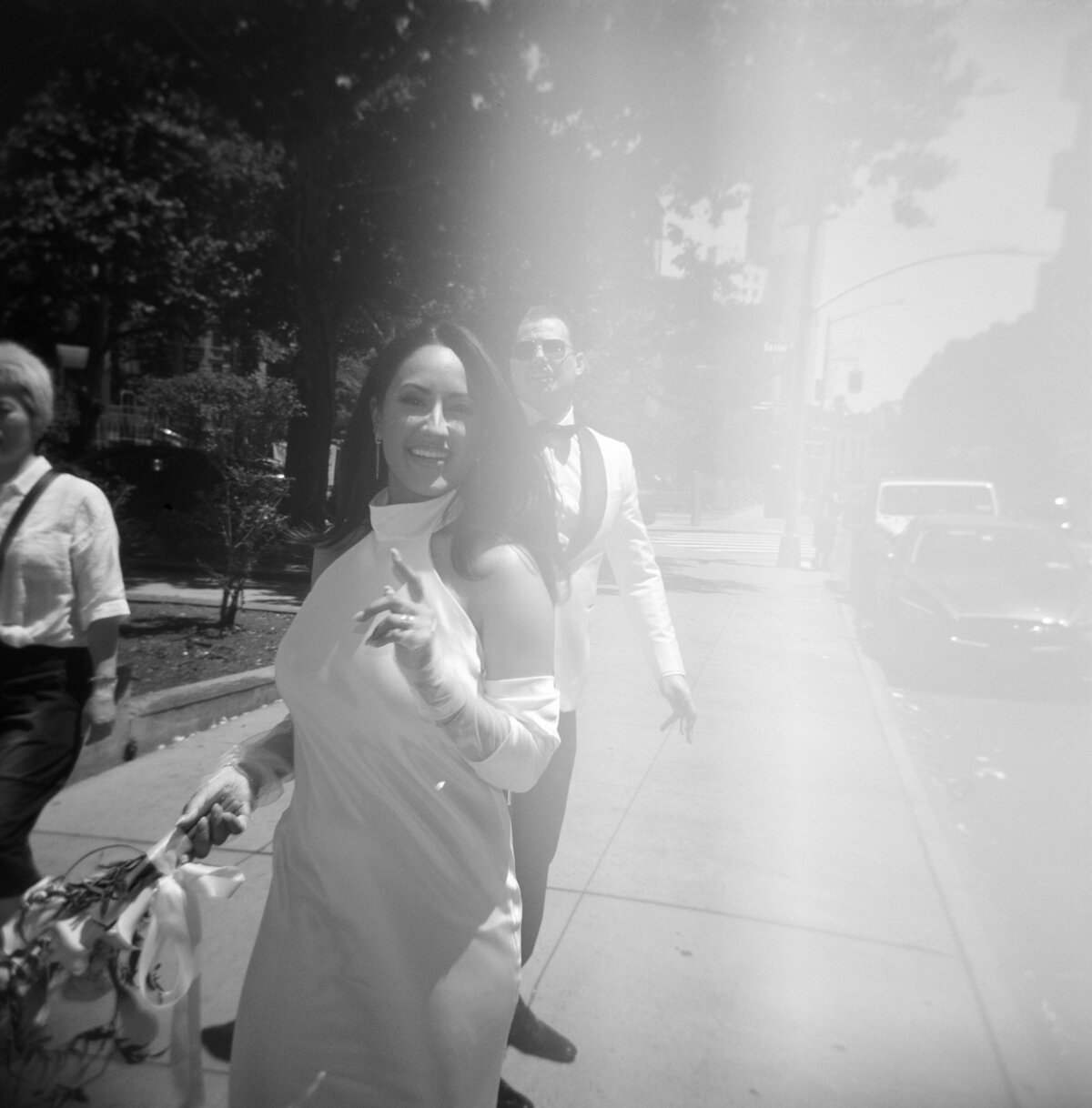 Black and white film photo with light leak of bride and groom walking joyfully through the streets of New York City during Japna and Chris’s Hotel Chelsea elopement, captured by NYC wedding photographer Perry Hancock.