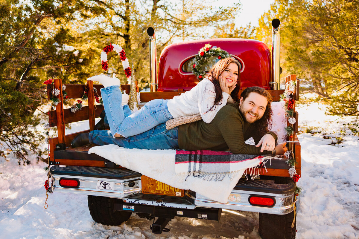 A teen boy and girl pose in the bed of a vintage red truck decorated for Christmas during a mini photo session in Albuquerque