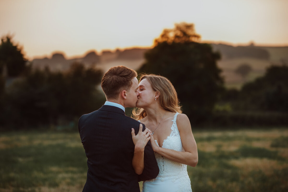 A bride and groom kissing at sunset