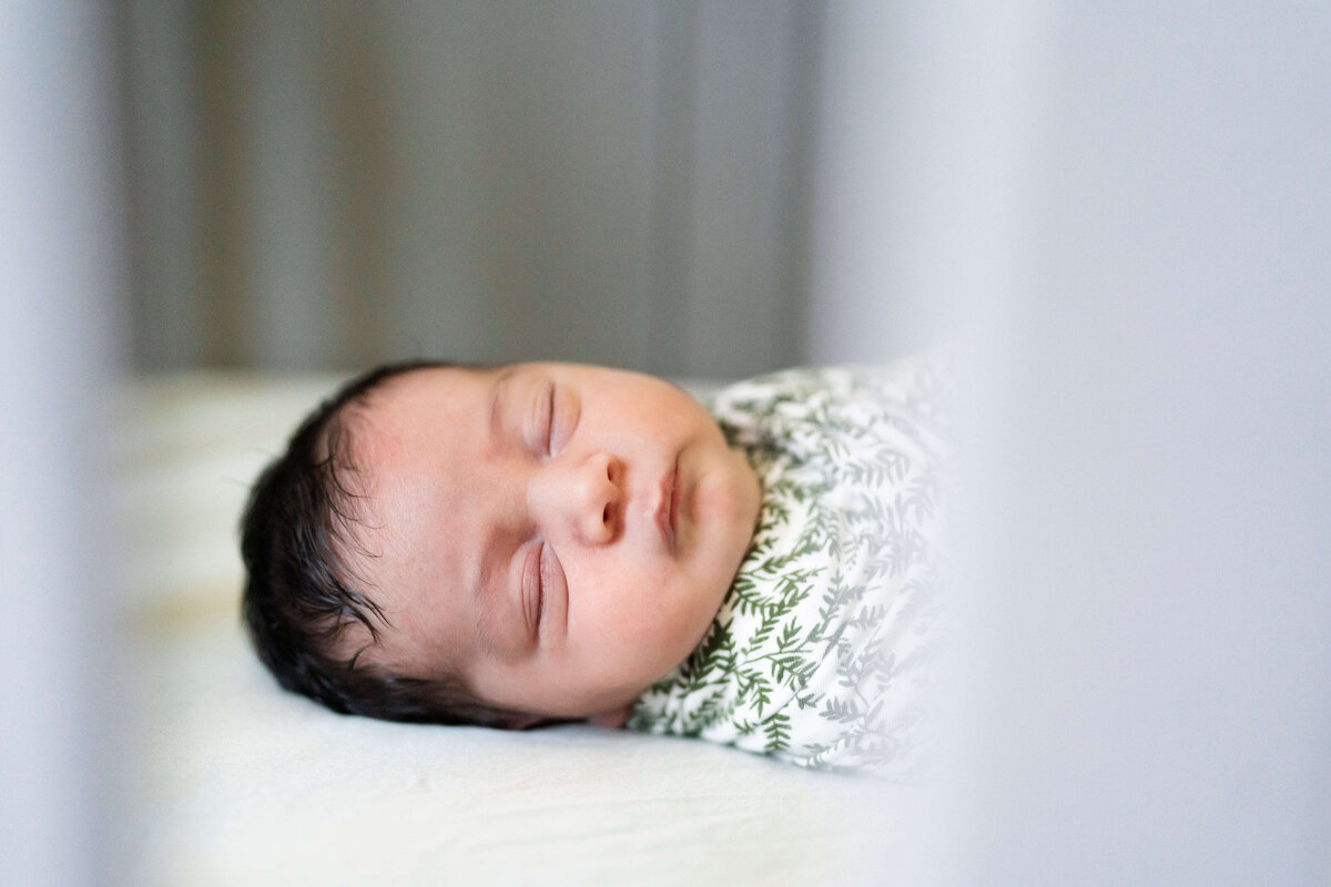 Newborn boy in crib facing camera with eyes closed