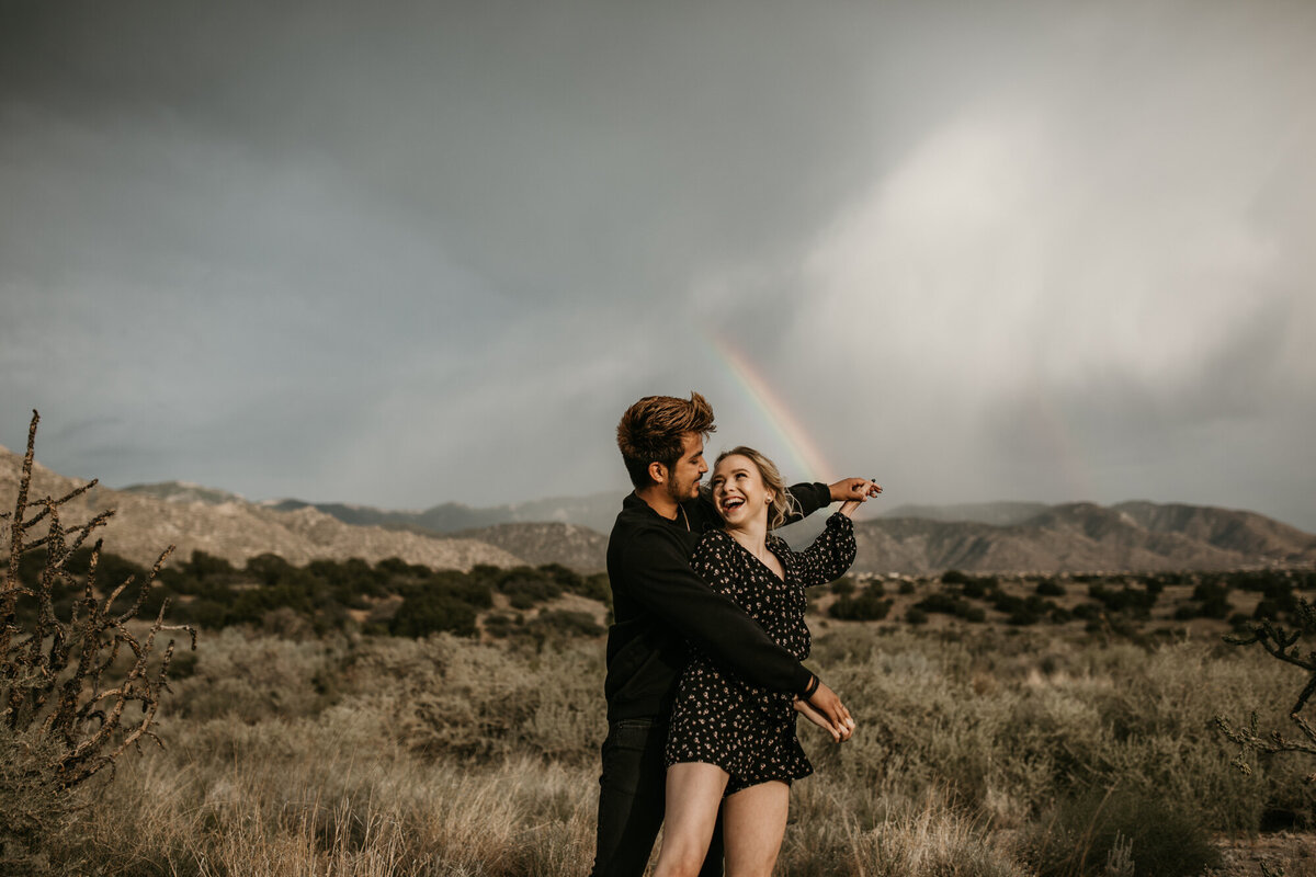 couple holding hands like airplane in front of a rainbow