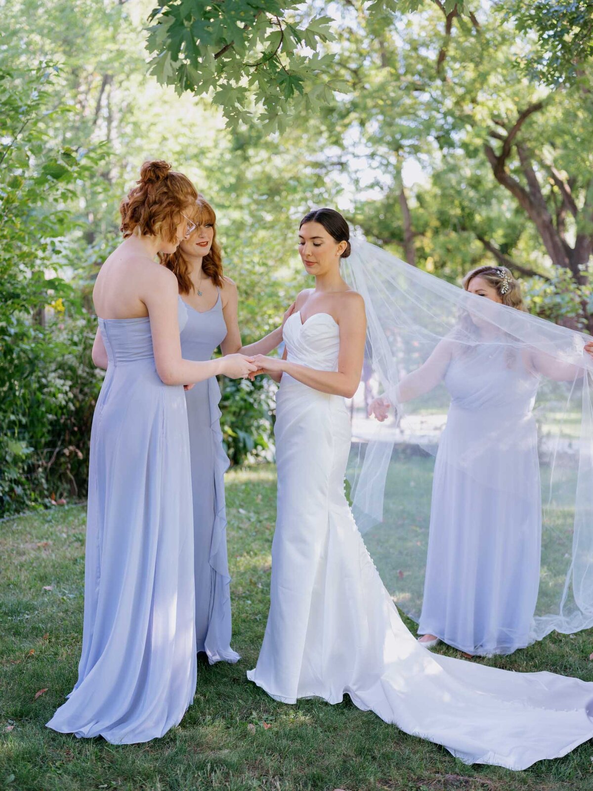 Bride in elegant Maggie Sottero gown surrouned by her bridesmaids in light blue Birdy Grey dresses