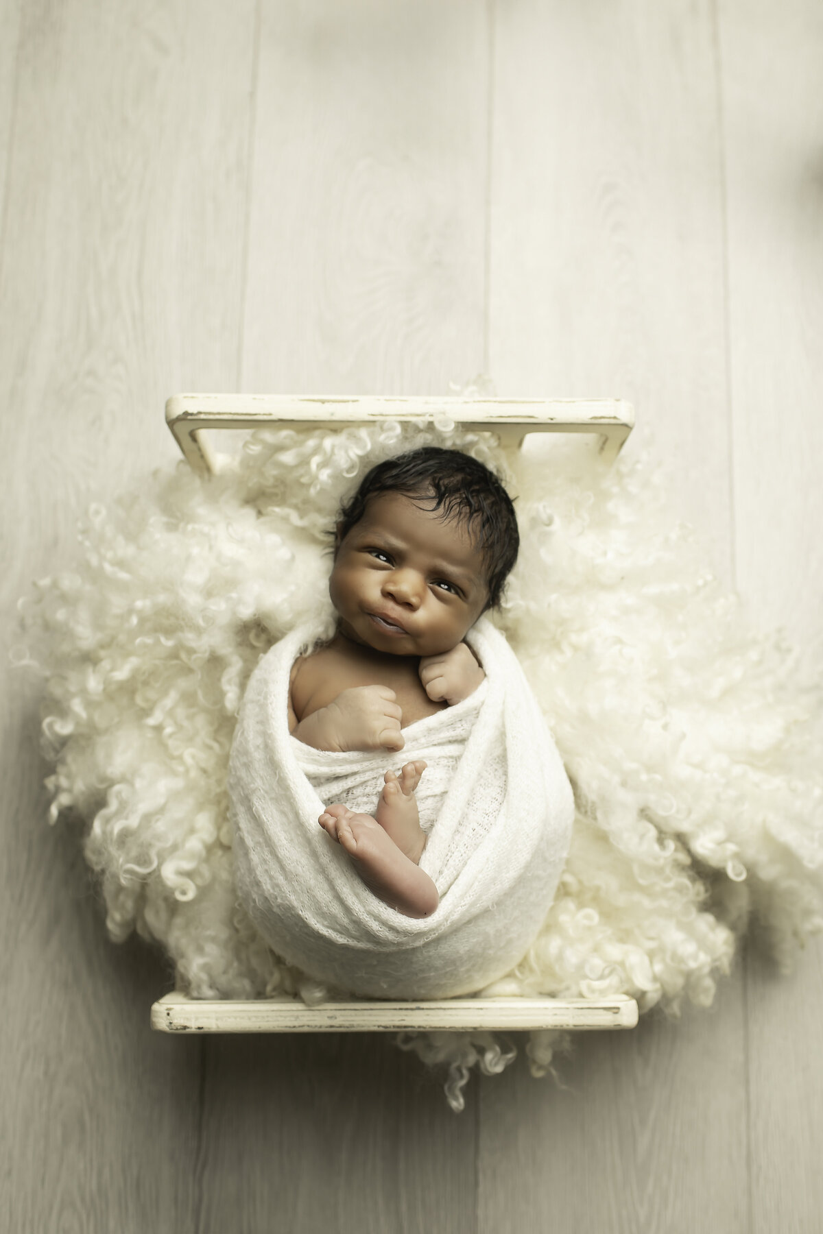 frican American newborn baby boy dressed in all white, peacefully lying on a bed, captured from an overhead angle, highlighting his delicate features in a soft and serene setting