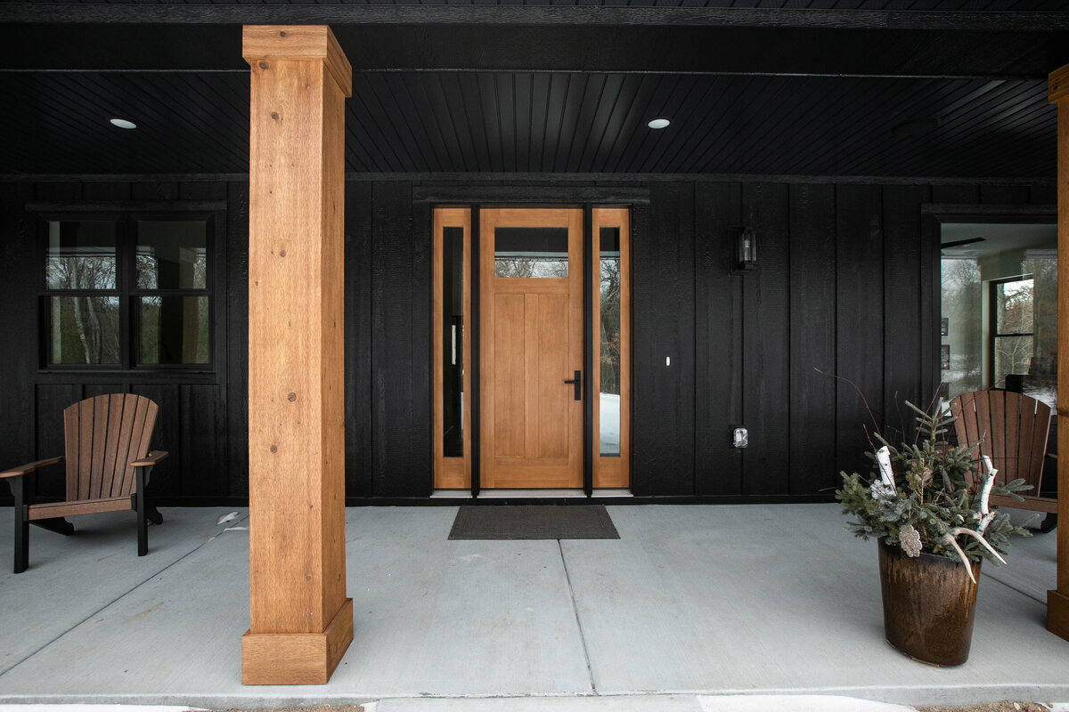 Exterior view of custom home in Elk River, Minnesota with black siding, wood details and front porch built by Cornerstone Custom Builds