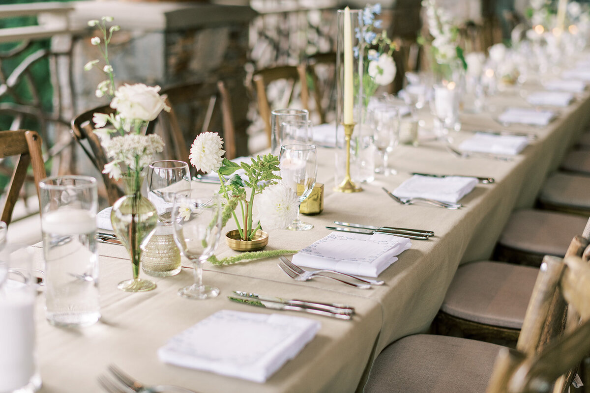 Long reception table with lush white and blue florals, taper candles, and gold votives at Trillium Links & Lake Club.