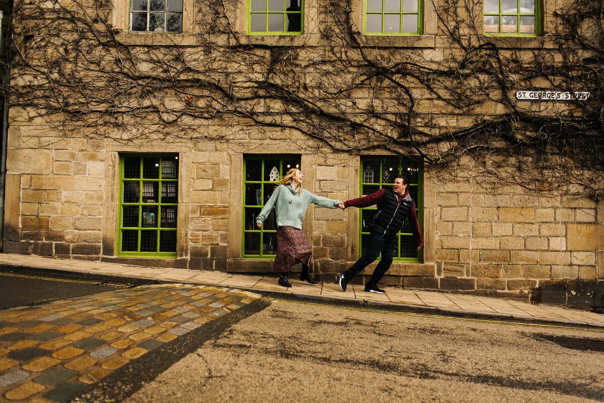 A couple on their pre wedding shoot running down the road holding hands in Hebden Bridge