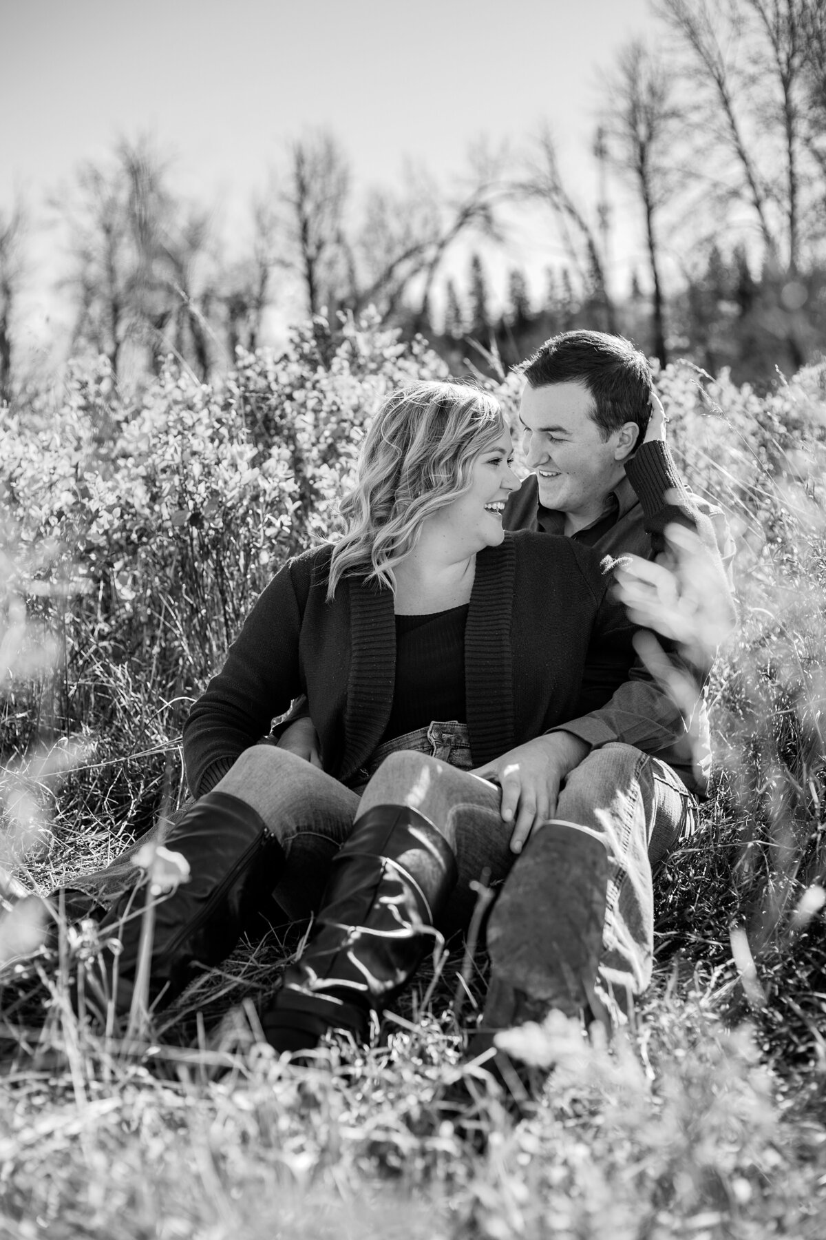 engaged-couple-sitting-in-field.-bw