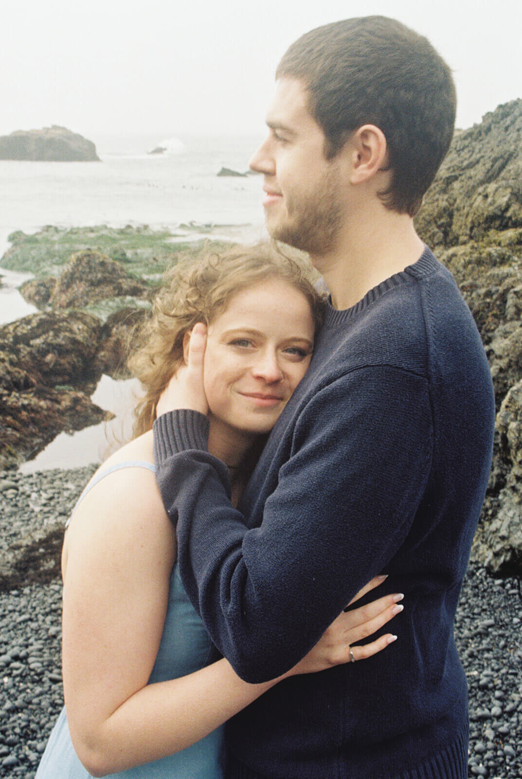 A woman smiles while embracing a man at the Oregon coast. 