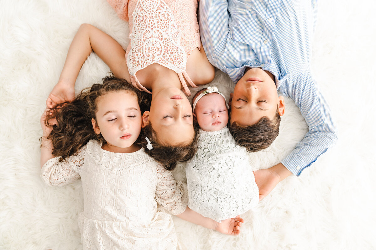 Four siblings snuggling on the floor in the studio, taken by Stickan Photography a Minneapolis Newborn Photographer