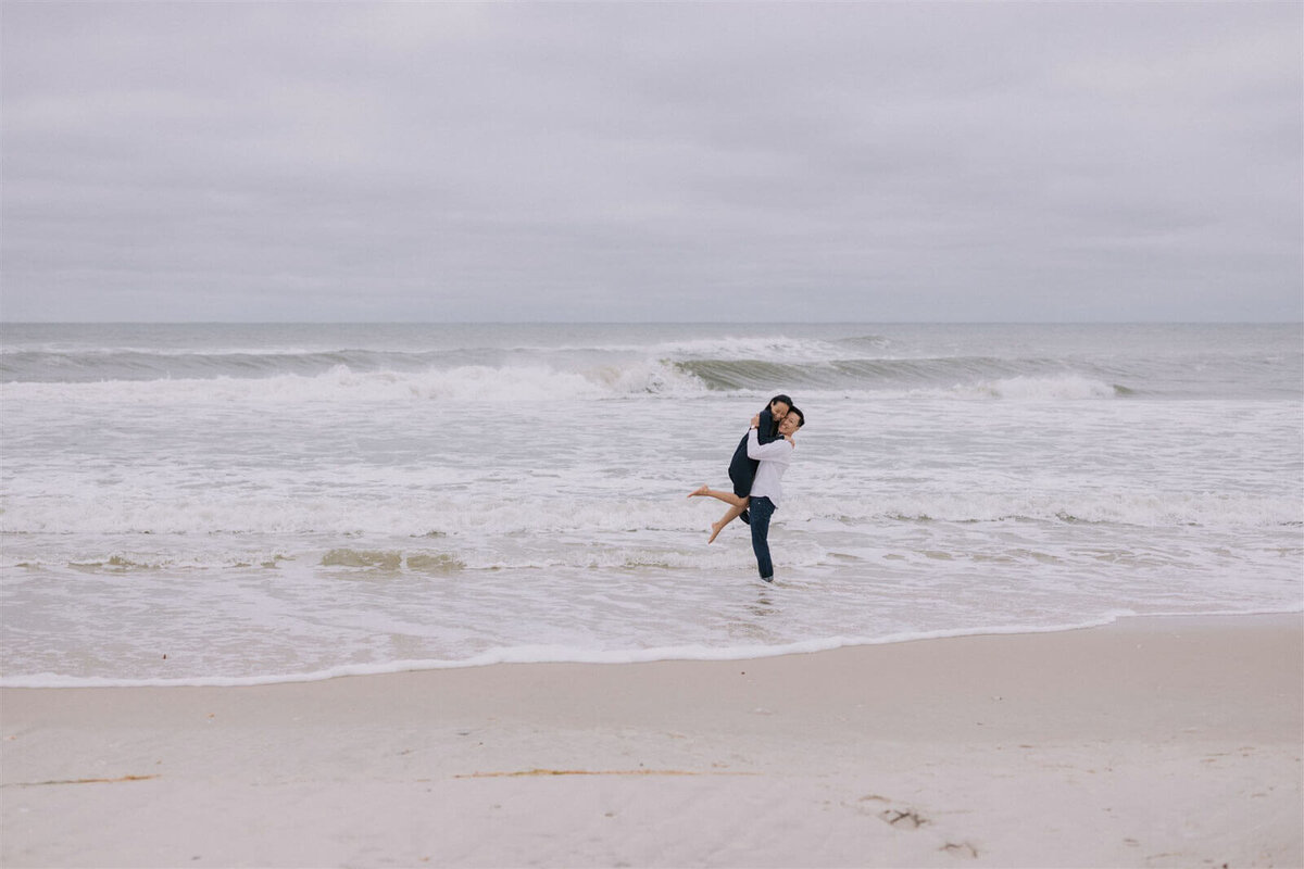 The man is happily carrying his fiancee on the waters of Fire Island Beach, NY. Engagement Image by Jenny Fu Studio