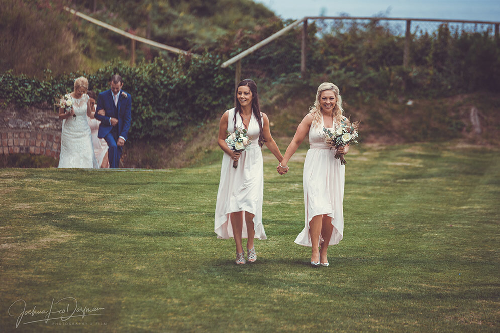 A couple of bridesmaids walking across a lush green lawn