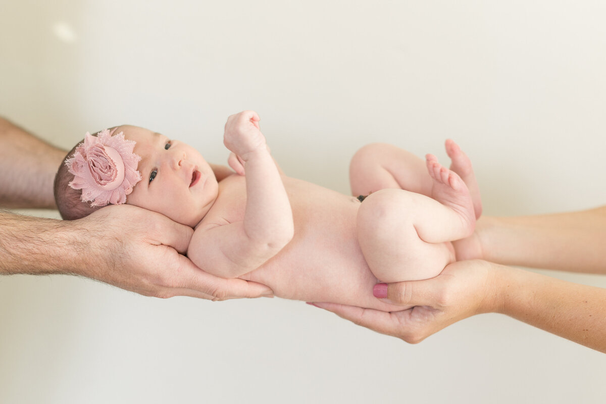 Two people's hands holding up a newborn baby