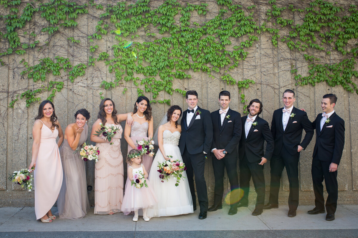 A wedding party poses outdoors in Montreal, in front of an ivy covered wall. 