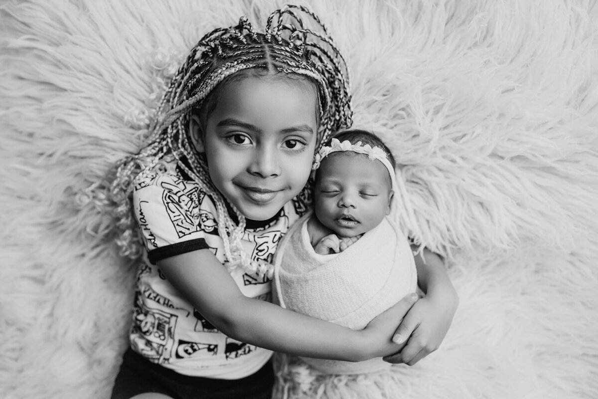 Black and white newborn photo with big sister snuggling her baby sister's head