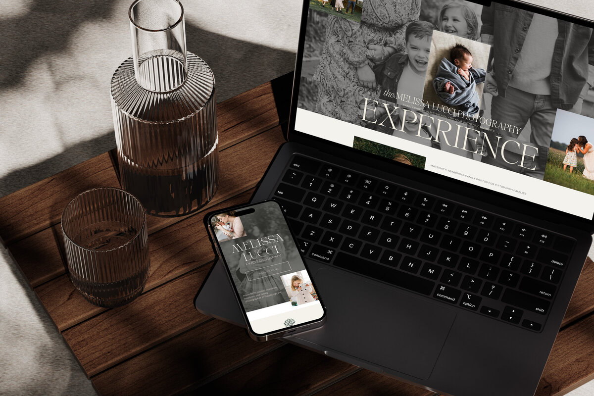 A laptop showcasing a photography website next to a smartphone on a wooden table with glassware; it’s clear that thoughtful brand strategy consulting was utilized.