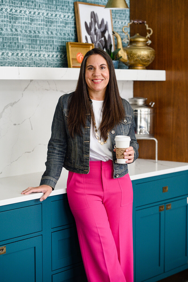 A denver personal branding photographer takes a photo of a woman leaning on the kitchen counter with coffee in her hand smiling for her Branding photos during a branding photography session.