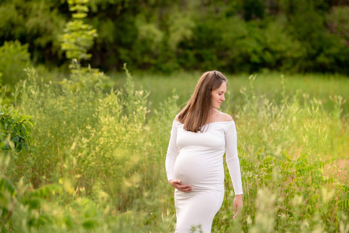 pregnant woman standing in a field holding her belly for her outdoor maternity photography session