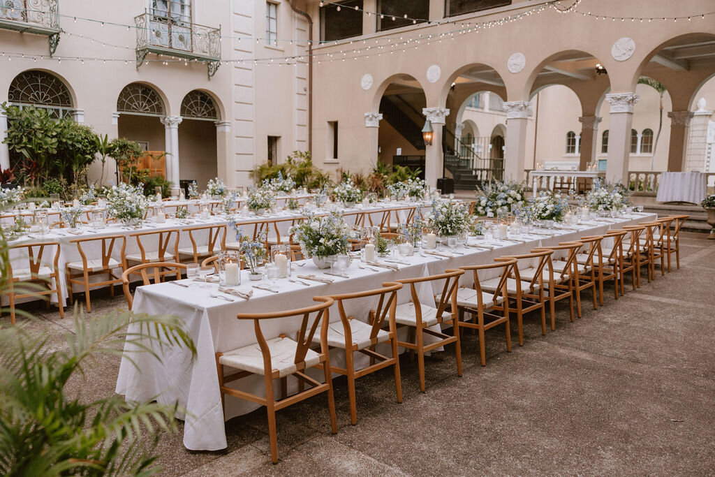 Dusky lighting with reception tables having blue and white florals on top in a courtyard